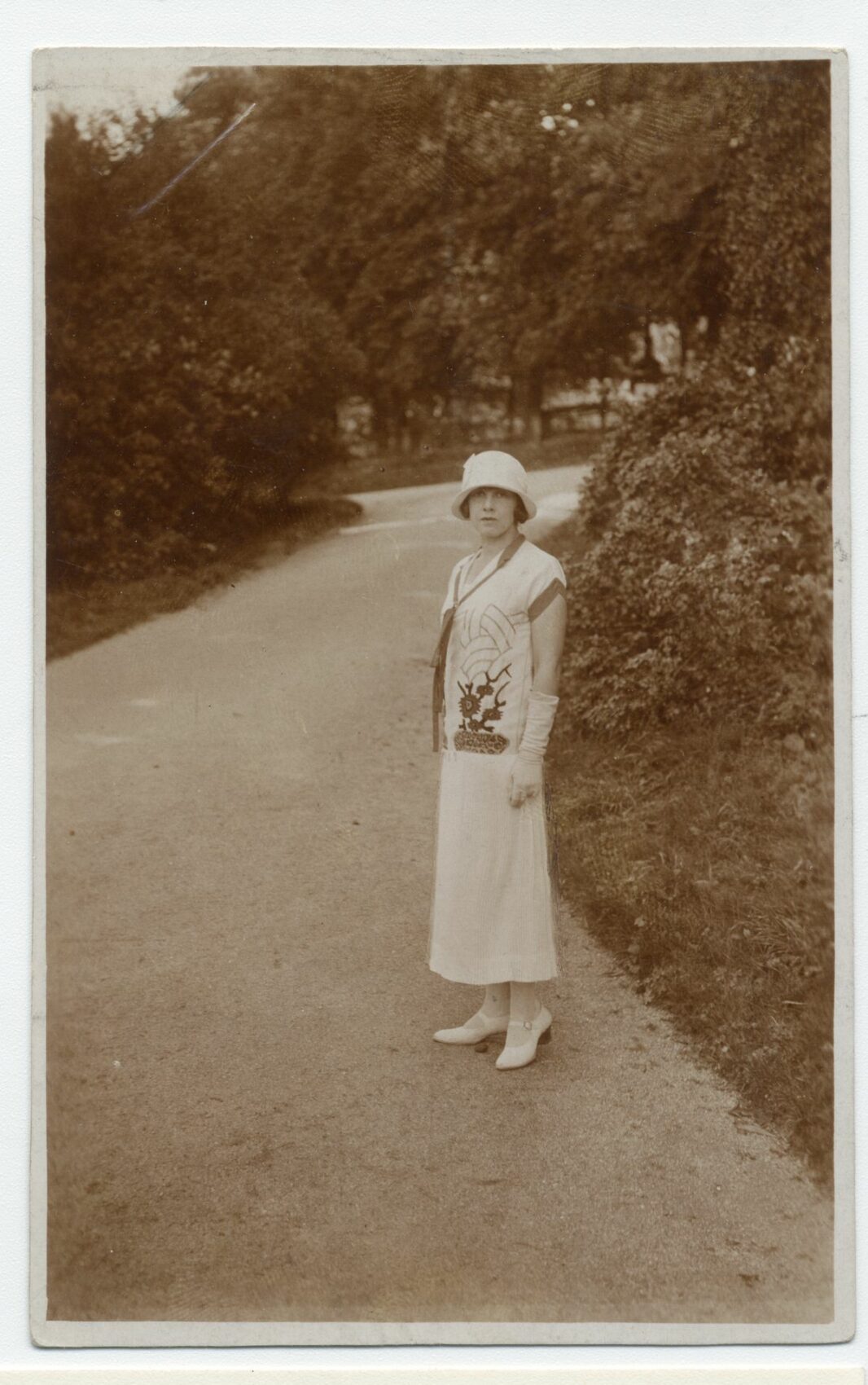 Fotografie mladé ženy v dlouhých světlých šatech s kloboučkem a vysokými rukavicemi