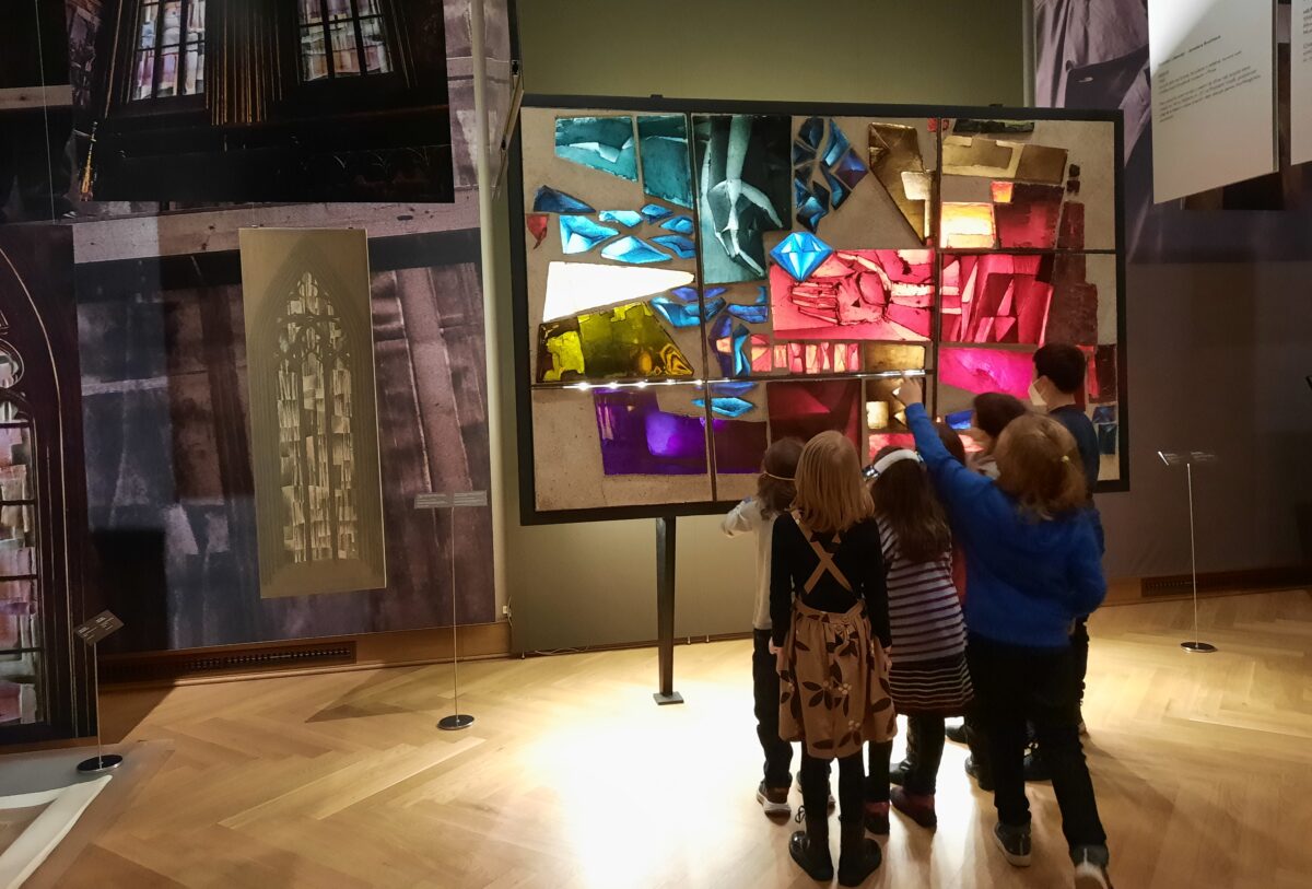 Skupinka dětí se dívá na barevnou skleněnou plastiku