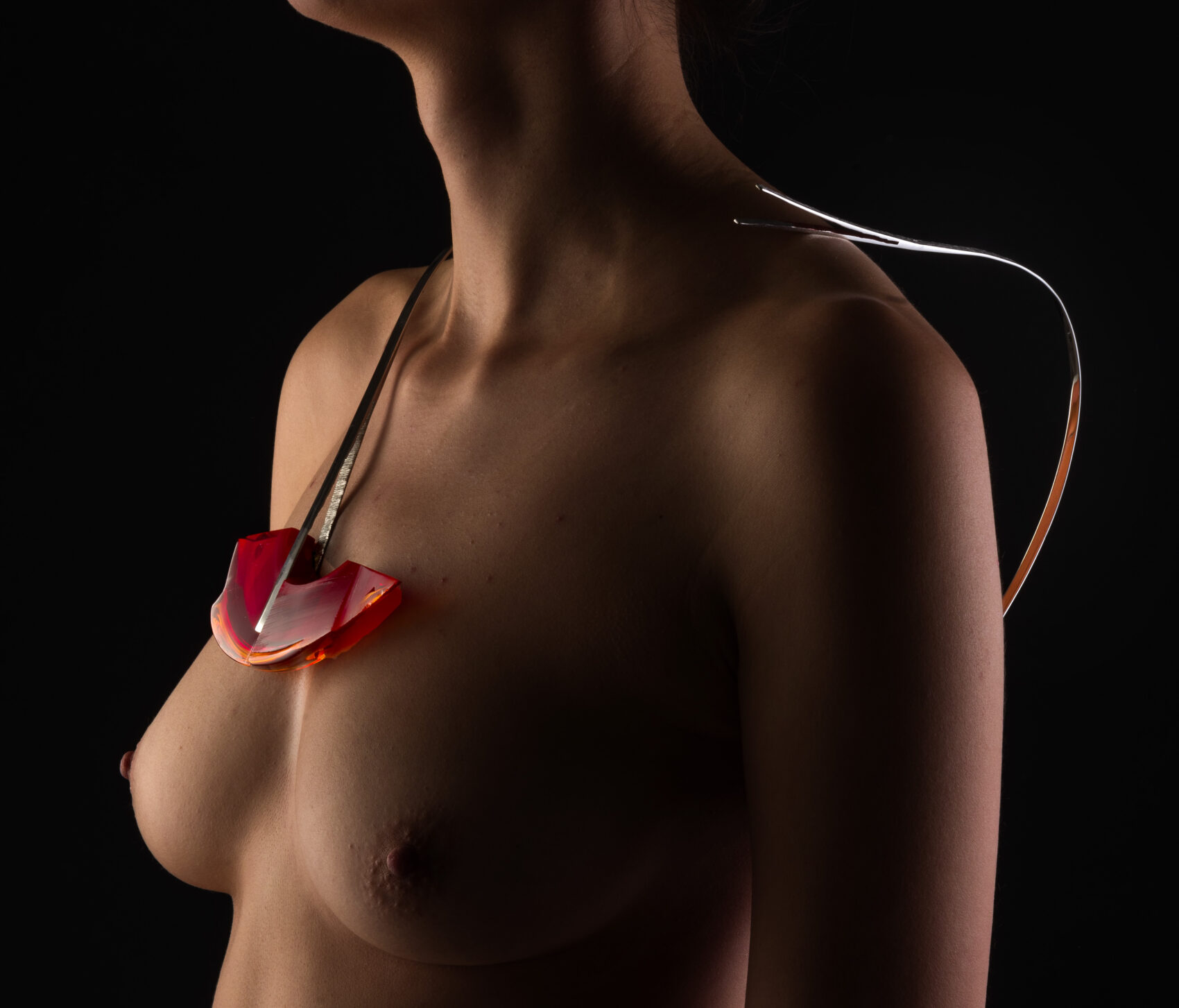 Červený skleněný náhrdelník na nahé ženské hrudi
